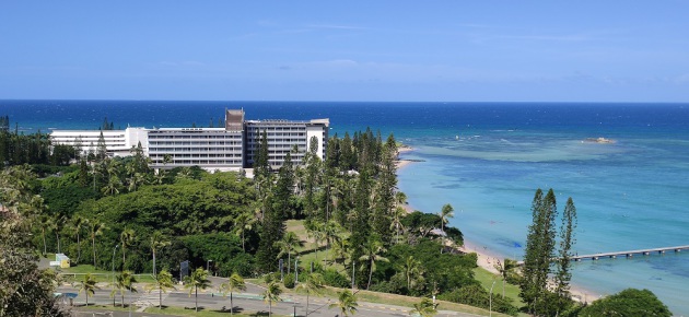 Au premier plan une route, au second plan un complexe hôtelier de plusieurs étages au pied de la plage, la mer au dernier plan.