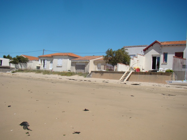 Photo prise depuis la plage, des maison sont à la limite du sable sec, parfois un muret marque la séparation du terrain et de la plage, parfois non.